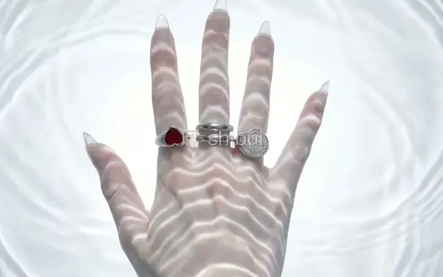 Mão com anéis e unhas compridas, sob luzes onduladas de água clara e brilhante.