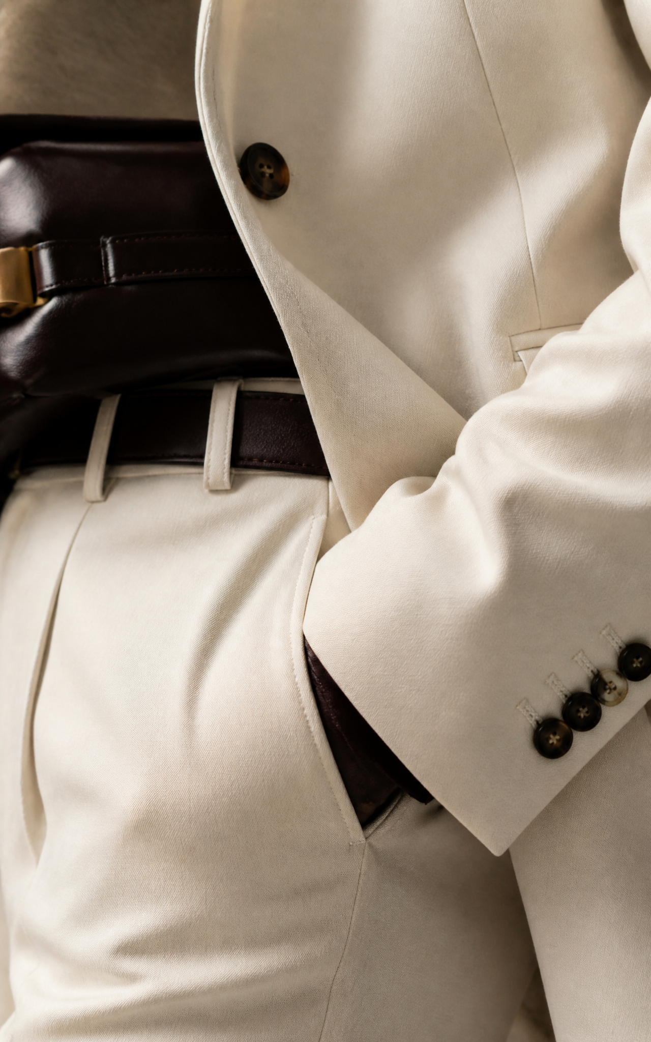 Close view of precise cream tailoring and dark leather accessories