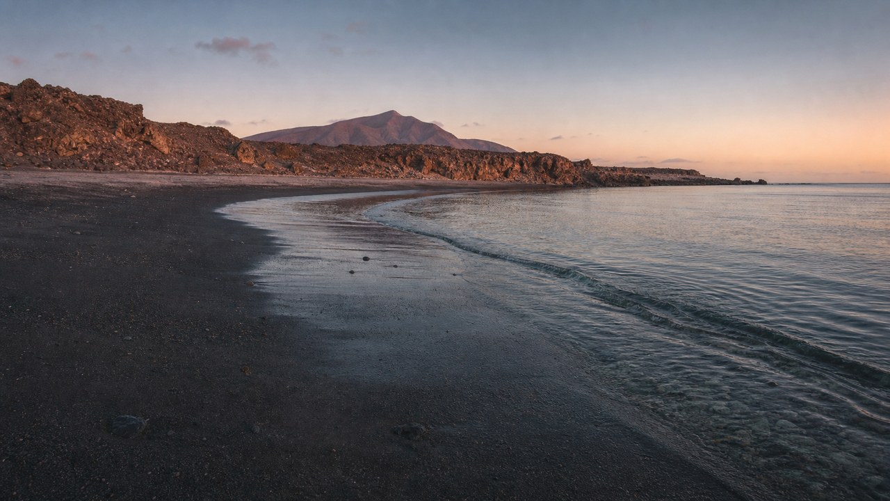 Dark volcanic sand meeting clear shallow water