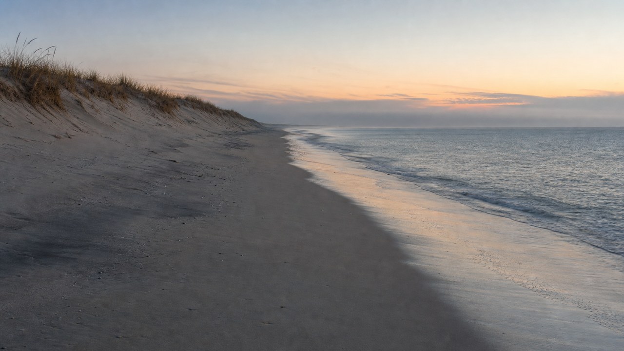 Pastel dusk light over calm water and low dunes