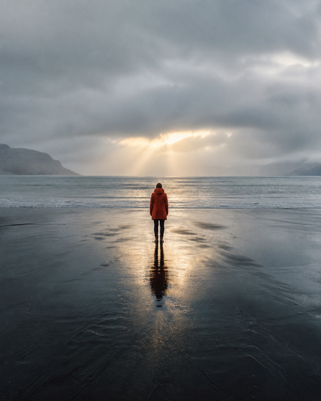 A solitary figure in a vermilion coat facing a luminous sea